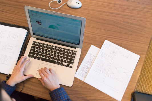 Person working on a laptop with printed documents on the desk