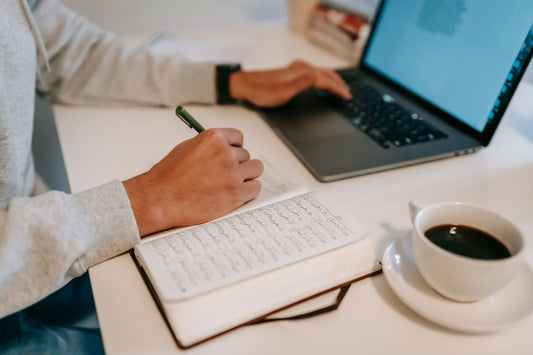 Freelance writer taking notes in a notebook while working on a laptop