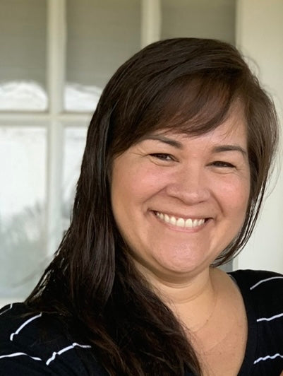 Smiling Hawaiian woman wearing a black and white striped tshirt in front of a beige wall and windows